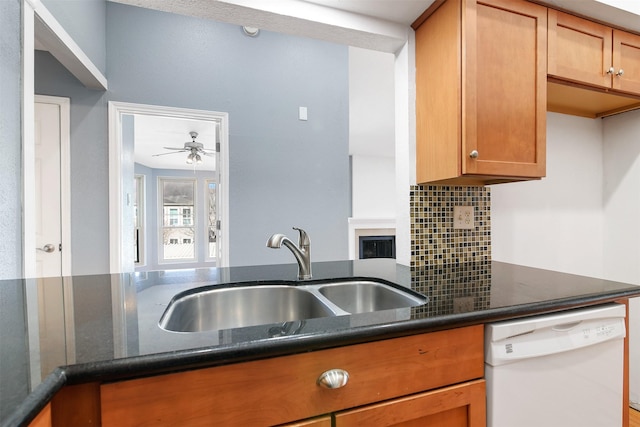 kitchen featuring tasteful backsplash, dark stone counters, brown cabinetry, dishwasher, and a sink