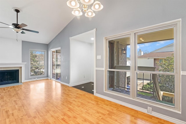 unfurnished living room featuring baseboards, a fireplace with flush hearth, wood finished floors, high vaulted ceiling, and ceiling fan with notable chandelier