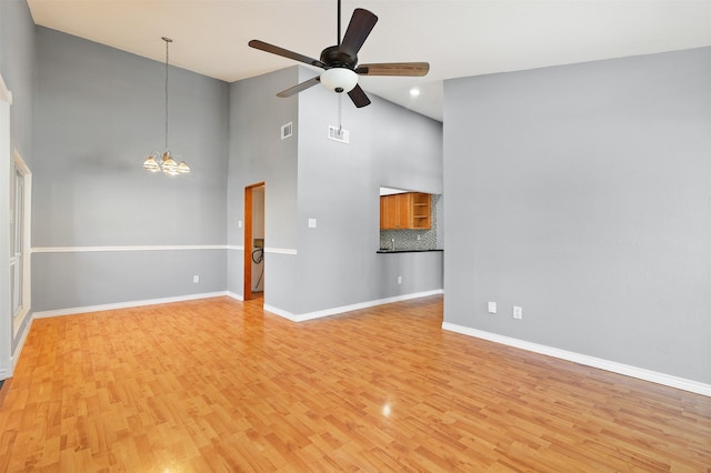 unfurnished living room with ceiling fan with notable chandelier, light wood-type flooring, visible vents, and baseboards