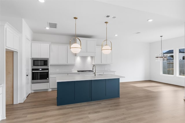 kitchen with tasteful backsplash, light wood-type flooring, appliances with stainless steel finishes, an island with sink, and white cabinets