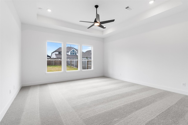 unfurnished room with light carpet, ceiling fan, and a tray ceiling