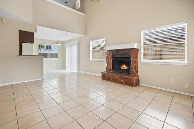 unfurnished living room with an inviting chandelier, a stone fireplace, a high ceiling, and light tile patterned floors