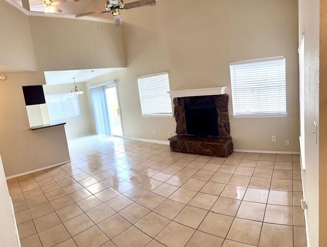 unfurnished living room featuring a high ceiling, a stone fireplace, ceiling fan with notable chandelier, and light tile patterned floors