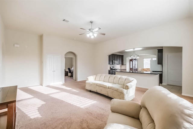 carpeted living room with ceiling fan with notable chandelier and sink