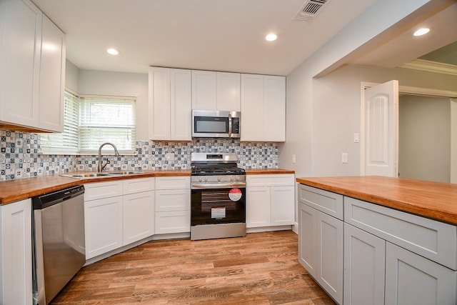 kitchen featuring light wood-style flooring, butcher block countertops, a sink, white cabinets, and appliances with stainless steel finishes