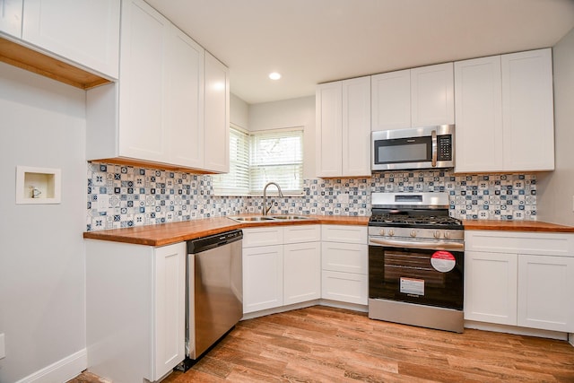 kitchen with appliances with stainless steel finishes, white cabinetry, a sink, wood counters, and light wood-type flooring