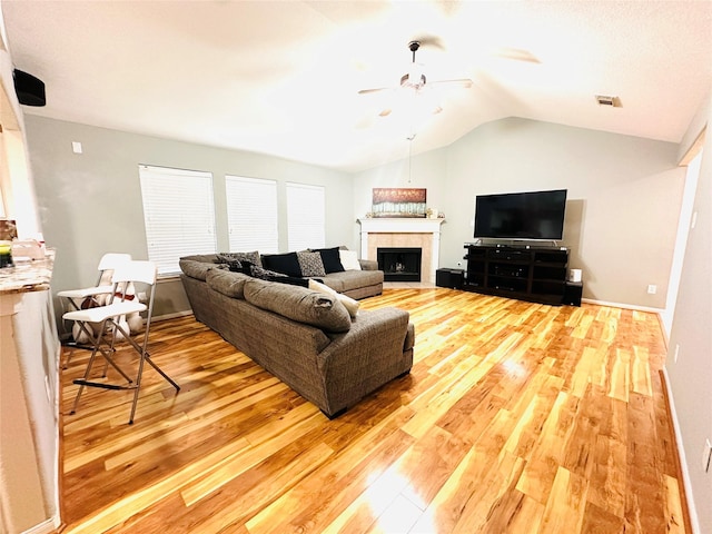 living room with a tiled fireplace, vaulted ceiling, and hardwood / wood-style floors