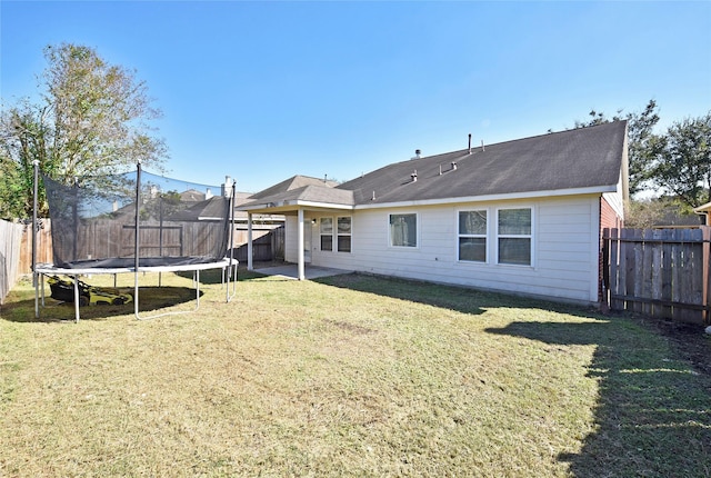 back of house with a trampoline and a lawn