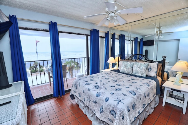 bedroom with a water view, dark tile patterned flooring, a textured ceiling, and access to outside