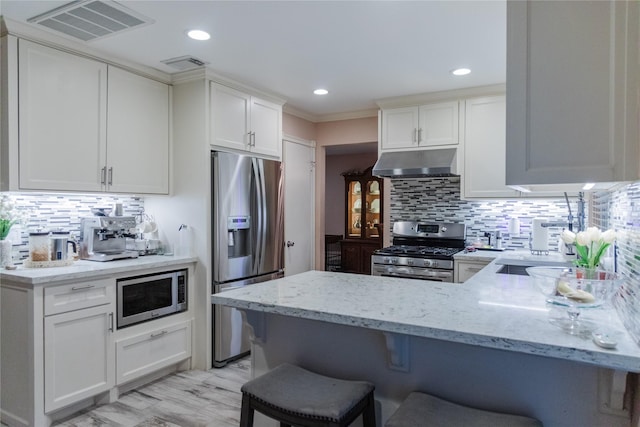 kitchen with a breakfast bar, appliances with stainless steel finishes, kitchen peninsula, light stone countertops, and white cabinets