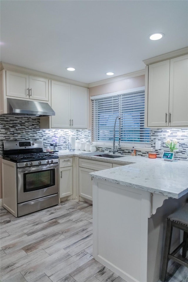 kitchen with sink, a breakfast bar area, white cabinets, gas range, and kitchen peninsula