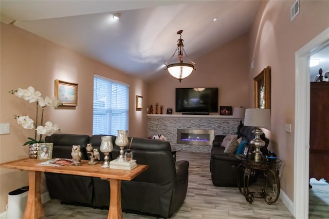 living room with vaulted ceiling, a stone fireplace, and light hardwood / wood-style flooring