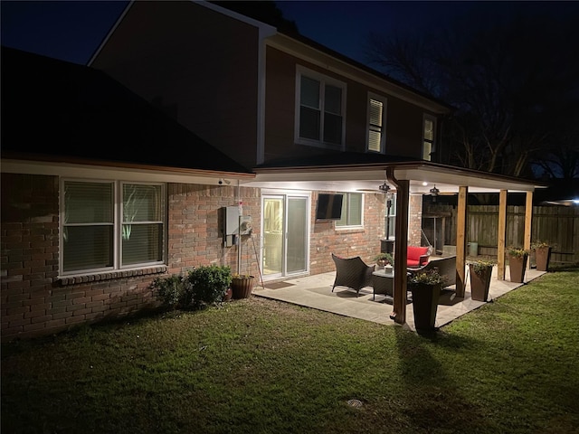 back house at twilight featuring a patio and a lawn