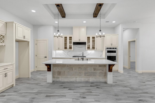 kitchen with hanging light fixtures, a chandelier, an island with sink, decorative backsplash, and beamed ceiling