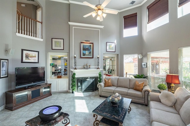 living room featuring a healthy amount of sunlight, light tile patterned flooring, ornamental molding, and a glass covered fireplace