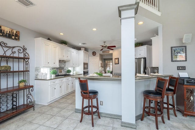 kitchen with a peninsula, visible vents, white cabinets, appliances with stainless steel finishes, and a kitchen bar