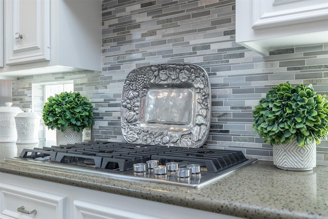 room details with tasteful backsplash, light stone countertops, white cabinets, and stainless steel gas stovetop