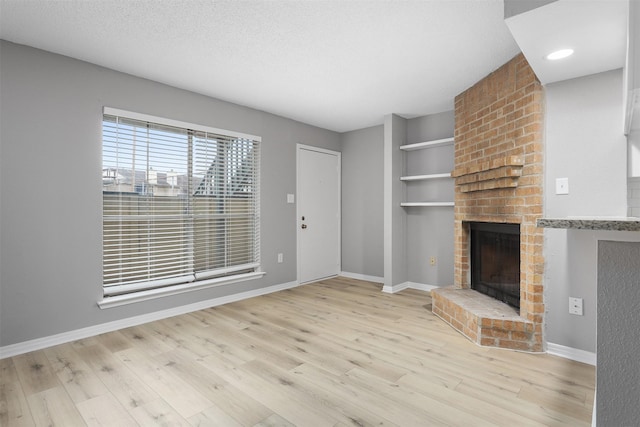 unfurnished living room featuring a textured ceiling, a brick fireplace, and light wood-type flooring