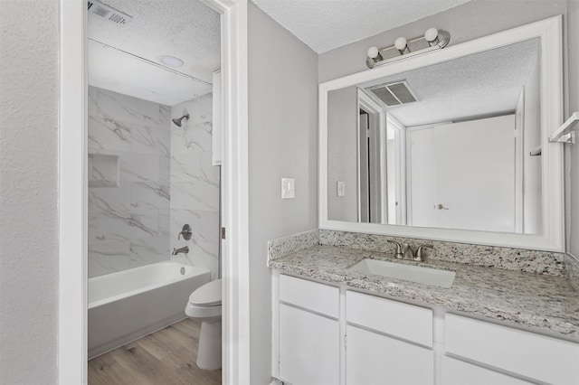 full bathroom featuring toilet, a textured ceiling, vanity, tiled shower / bath combo, and hardwood / wood-style flooring