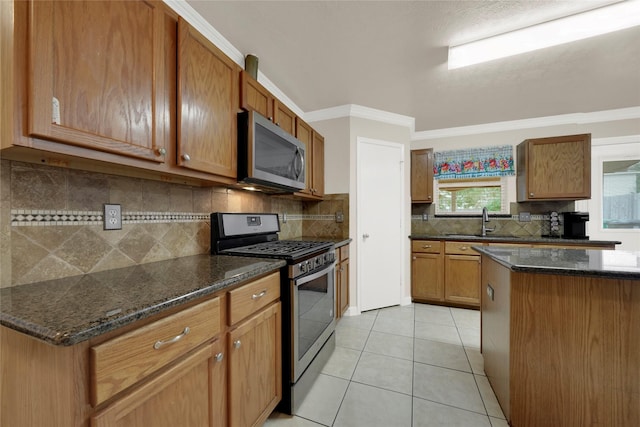 kitchen featuring sink, light tile patterned floors, dark stone counters, and appliances with stainless steel finishes