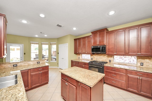 kitchen featuring light tile patterned flooring, decorative backsplash, reddish brown cabinets, stainless steel microwave, and gas stove