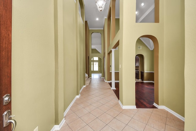 hallway with arched walkways, light tile patterned floors, visible vents, a high ceiling, and baseboards