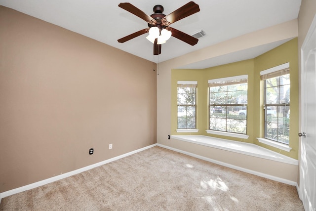 carpeted spare room featuring a healthy amount of sunlight, baseboards, visible vents, and a ceiling fan