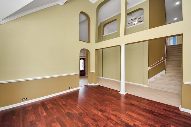 empty room featuring baseboards, arched walkways, wood finished floors, a high ceiling, and stairs