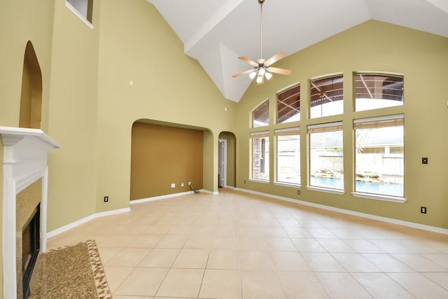 unfurnished living room featuring baseboards, arched walkways, ceiling fan, a fireplace, and light tile patterned flooring