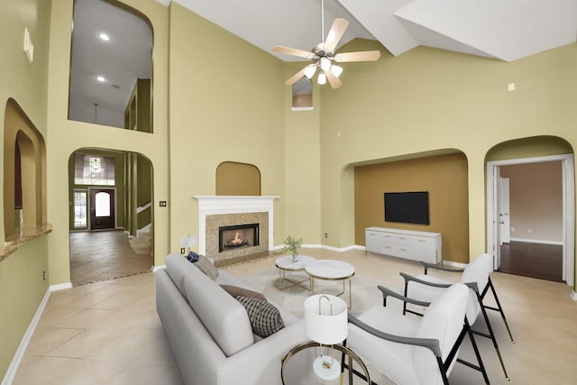 living area with light tile patterned floors, baseboards, arched walkways, high vaulted ceiling, and a high end fireplace