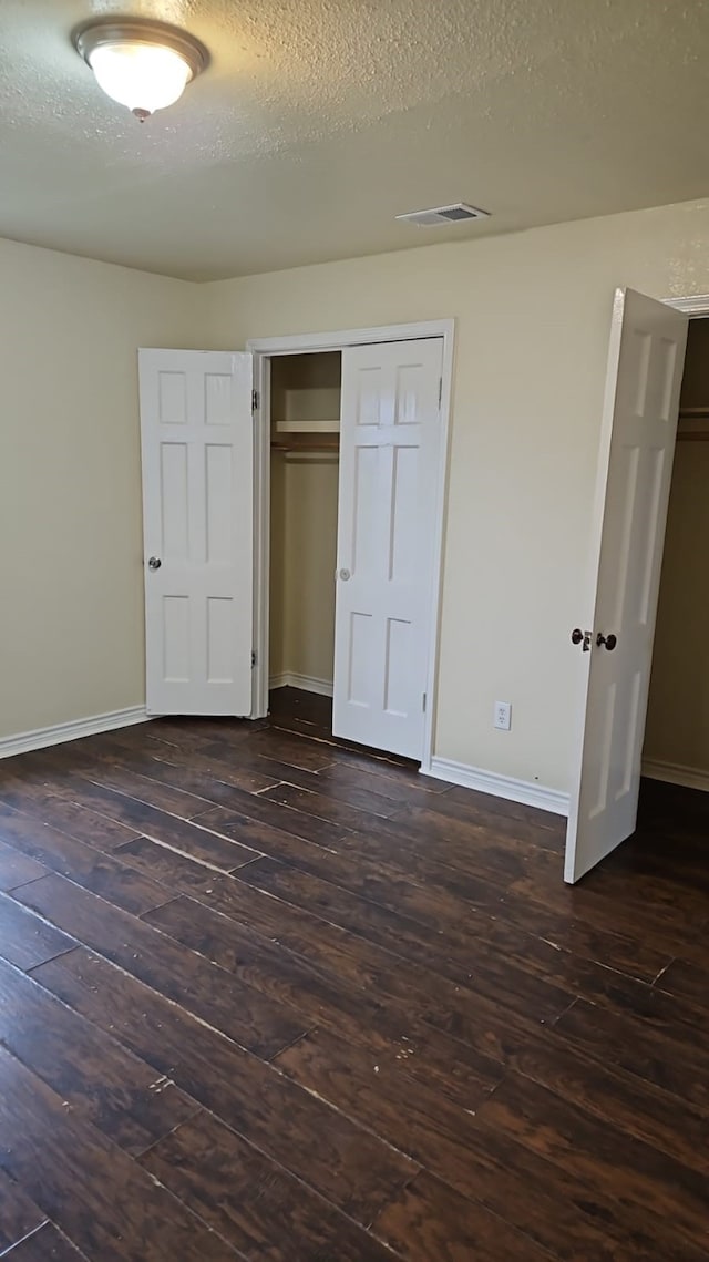 unfurnished bedroom with a textured ceiling and dark hardwood / wood-style flooring