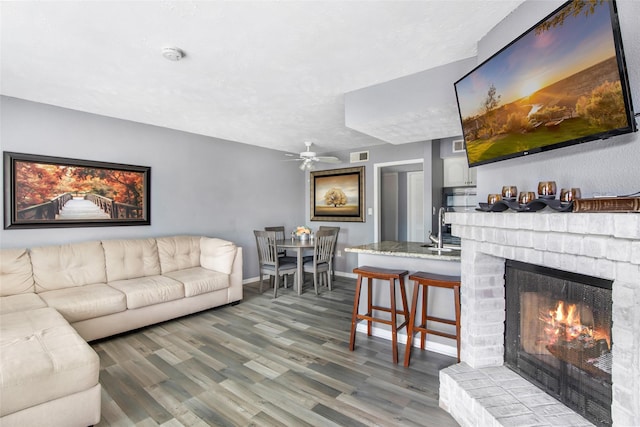 living room featuring ceiling fan, wood-type flooring, sink, and a brick fireplace