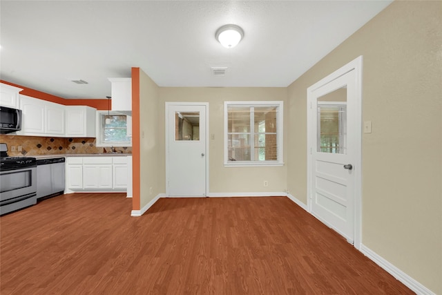 kitchen with hardwood / wood-style flooring, appliances with stainless steel finishes, backsplash, and white cabinets