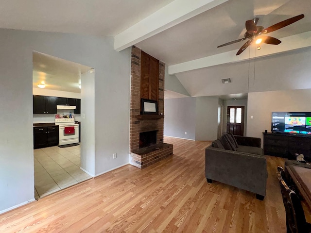 living room featuring a brick fireplace, vaulted ceiling with beams, ceiling fan, and light wood-type flooring