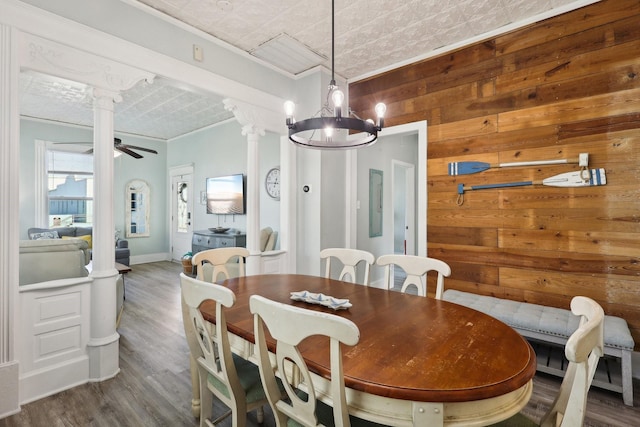 dining space featuring decorative columns, wooden walls, crown molding, and ceiling fan with notable chandelier