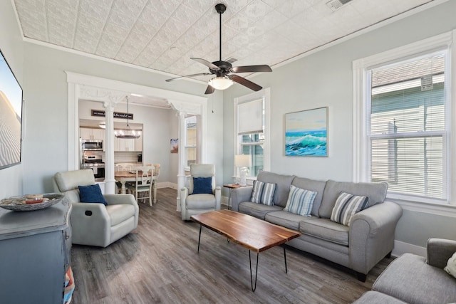 living room featuring baseboards, an ornate ceiling, wood finished floors, crown molding, and ceiling fan with notable chandelier