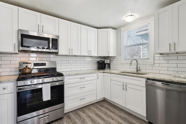 kitchen with light wood finished floors, appliances with stainless steel finishes, a sink, white cabinetry, and backsplash