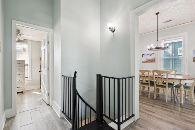 corridor with baseboards, visible vents, wood finished floors, an upstairs landing, and a notable chandelier