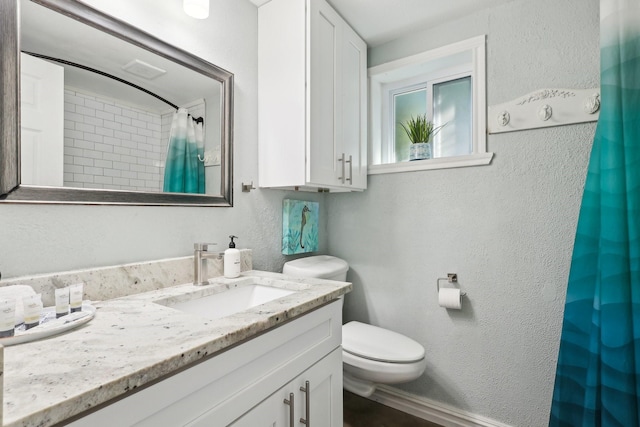 bathroom featuring curtained shower, a textured wall, vanity, and toilet