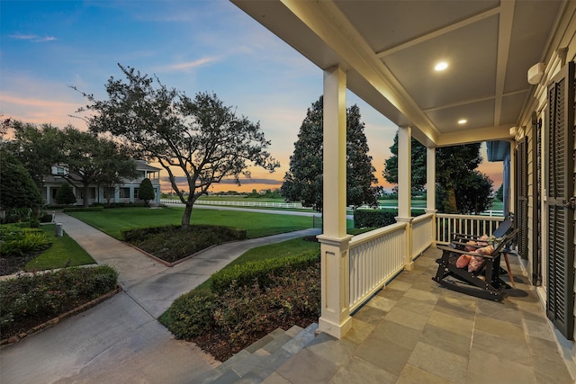 patio terrace at dusk with covered porch and a lawn