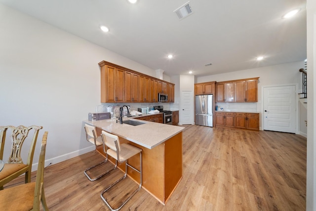 kitchen featuring sink, a breakfast bar area, light wood-type flooring, kitchen peninsula, and stainless steel appliances