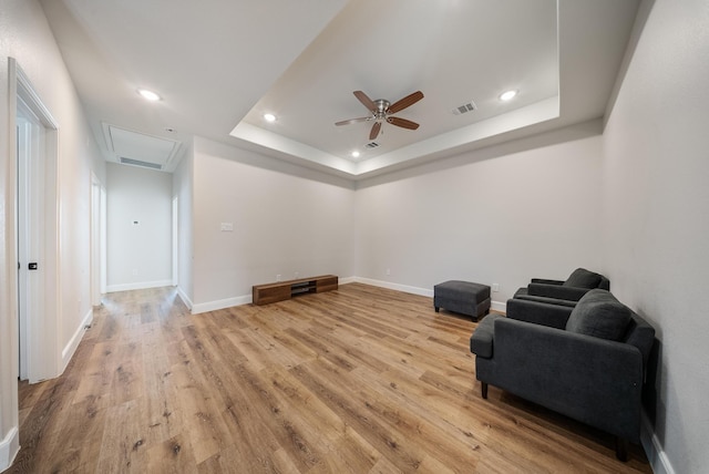 living area with ceiling fan, light wood-type flooring, and a tray ceiling