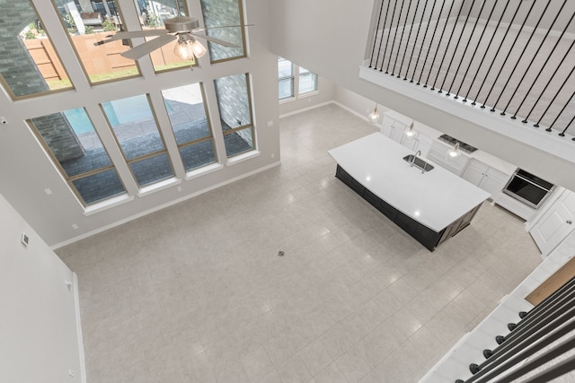 living area with baseboards, ceiling fan, a high ceiling, and stairs