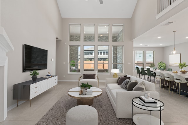 living room featuring ceiling fan, light tile patterned flooring, a high ceiling, visible vents, and baseboards