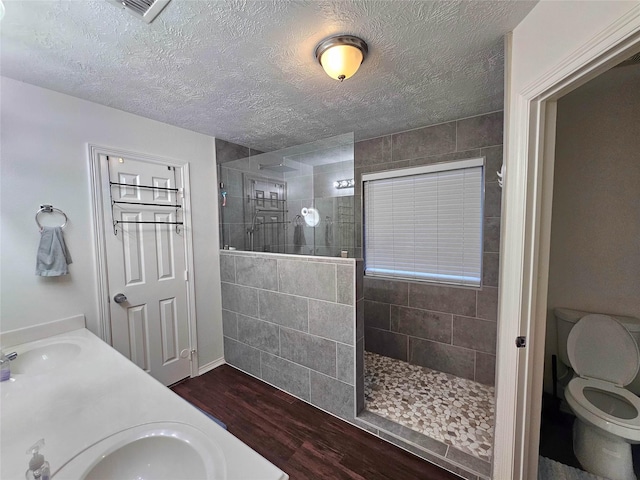 bathroom featuring hardwood / wood-style flooring, tiled shower, vanity, and toilet