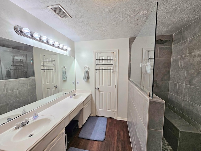 bathroom featuring hardwood / wood-style flooring, vanity, a tile shower, and a textured ceiling