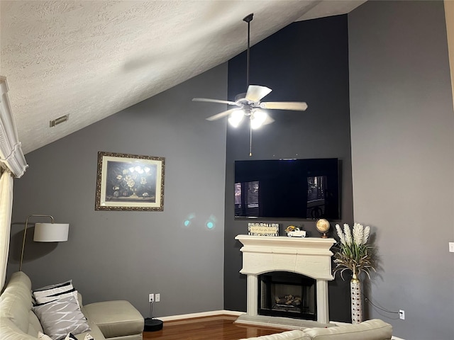 living area featuring a fireplace with raised hearth, ceiling fan, wood finished floors, vaulted ceiling, and a textured ceiling