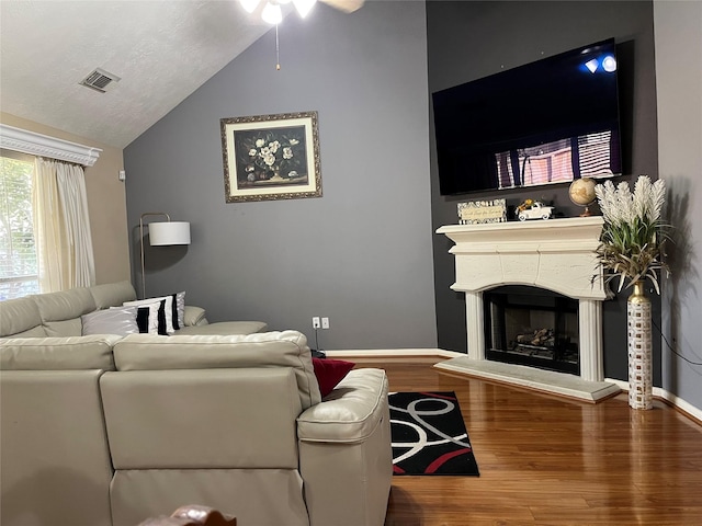 living area with baseboards, visible vents, a fireplace with raised hearth, lofted ceiling, and wood finished floors