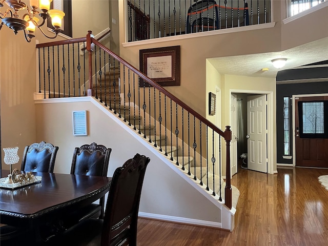 interior space featuring a towering ceiling, wood finished floors, a chandelier, baseboards, and stairs