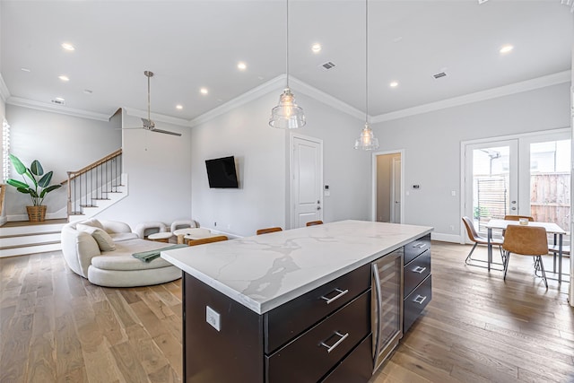 kitchen with crown molding, decorative light fixtures, a kitchen island, beverage cooler, and light hardwood / wood-style floors